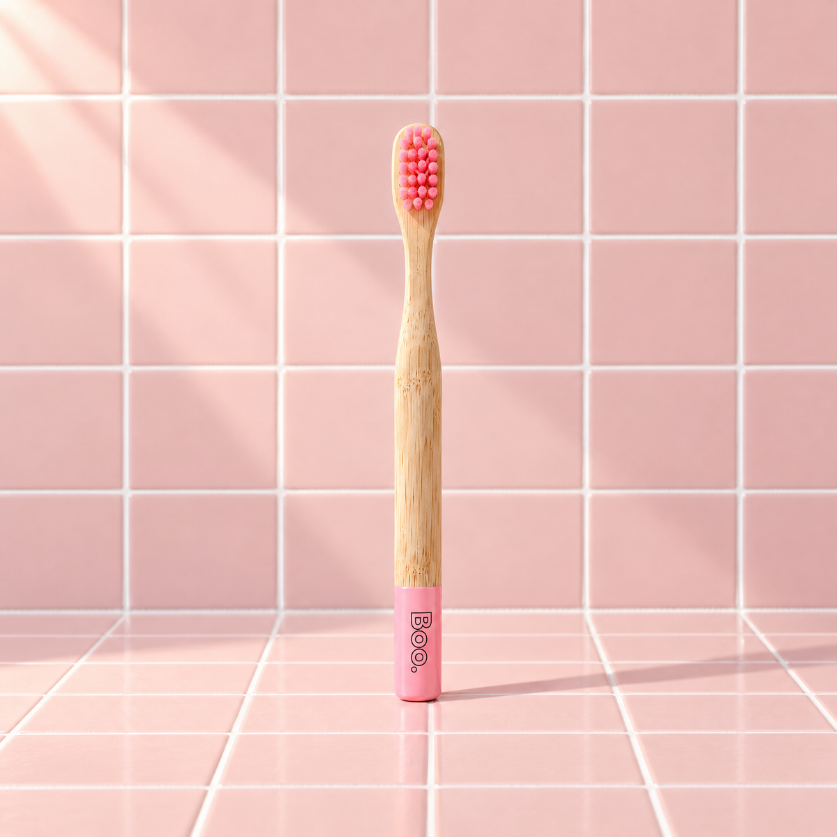 Boo kids bamboo toothbrush with pink bristles and a pink end cap, standing on pink tiles