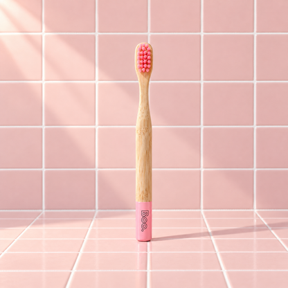Boo kids bamboo toothbrush with pink bristles and a pink end cap, standing on pink tiles