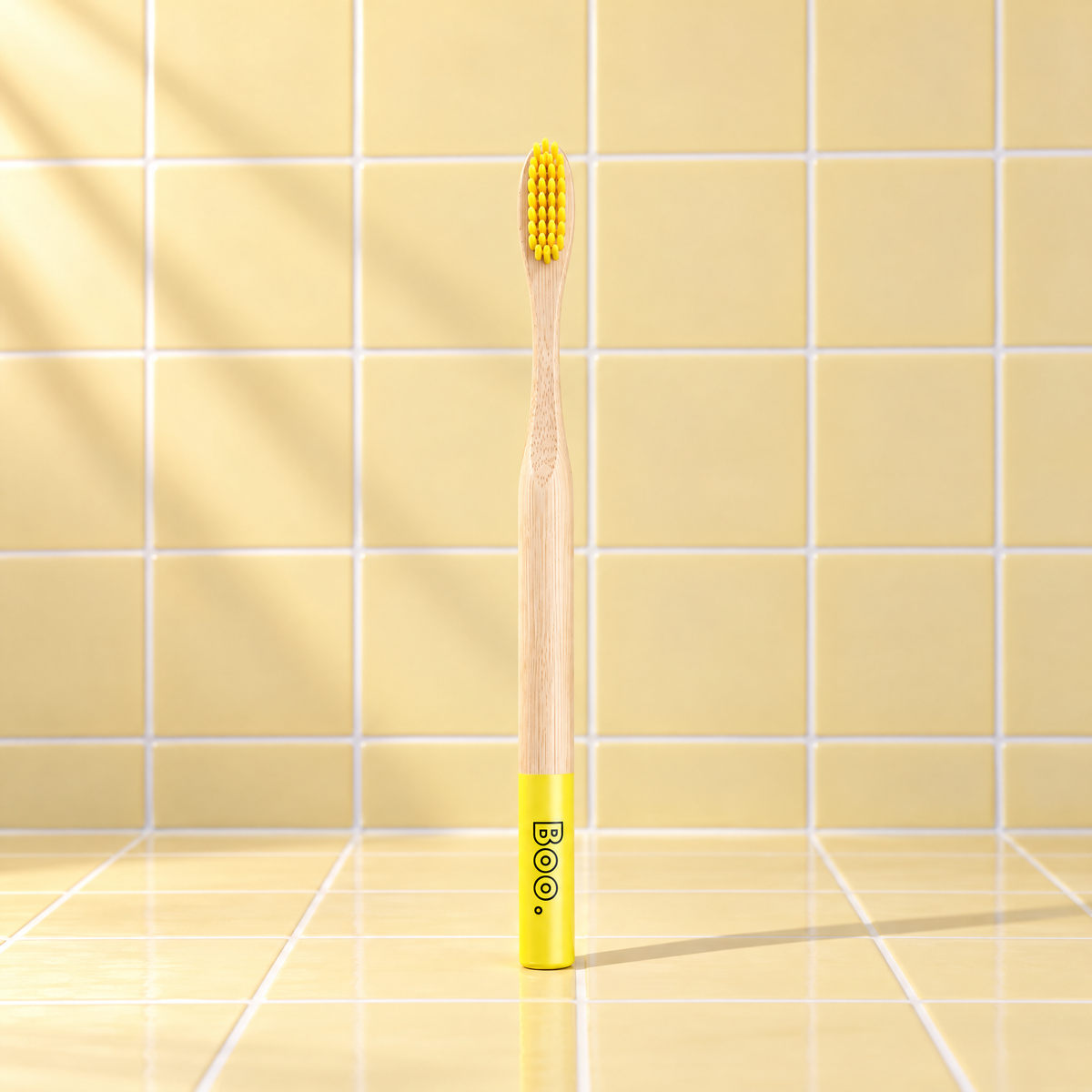 Boo adult bamboo toothbrush with yellow bristles and a yellow end cap, standing on yellow tiles