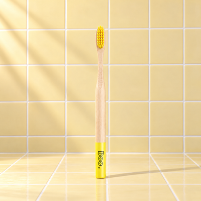 Boo adult bamboo toothbrush with yellow bristles and a yellow end cap, standing on yellow tiles
