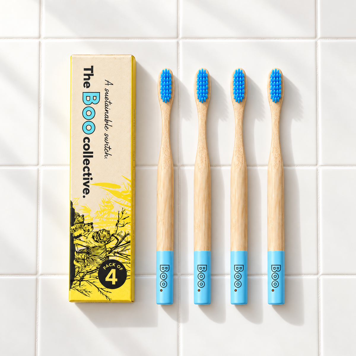 Four Boo adult bamboo toothbrushes with blue bristles laid out beside the Boo four pack box