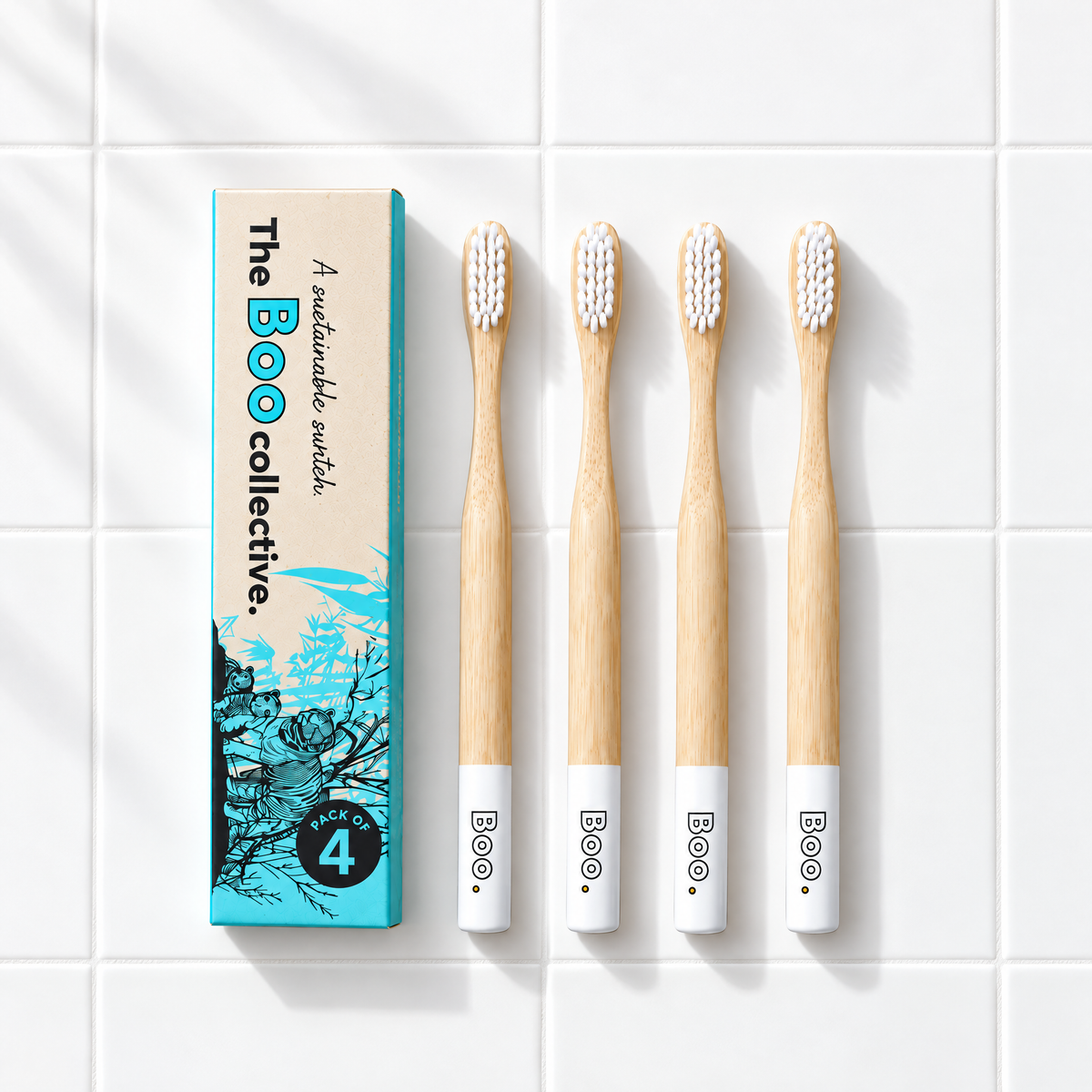 Four Boo adult bamboo toothbrushes with white bristles laid out beside the Boo four pack box