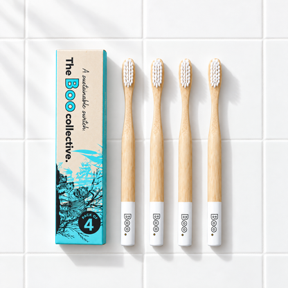 Four Boo adult bamboo toothbrushes with white bristles laid out beside the Boo four pack box