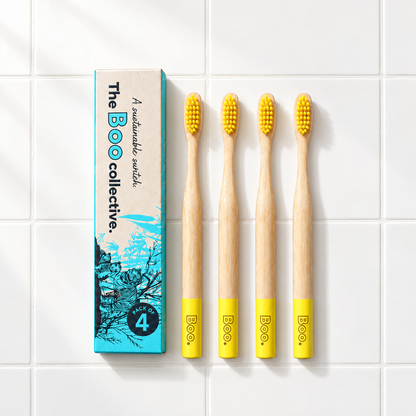 Four Boo adult bamboo toothbrushes with yellow bristles laid out beside the Boo four pack box