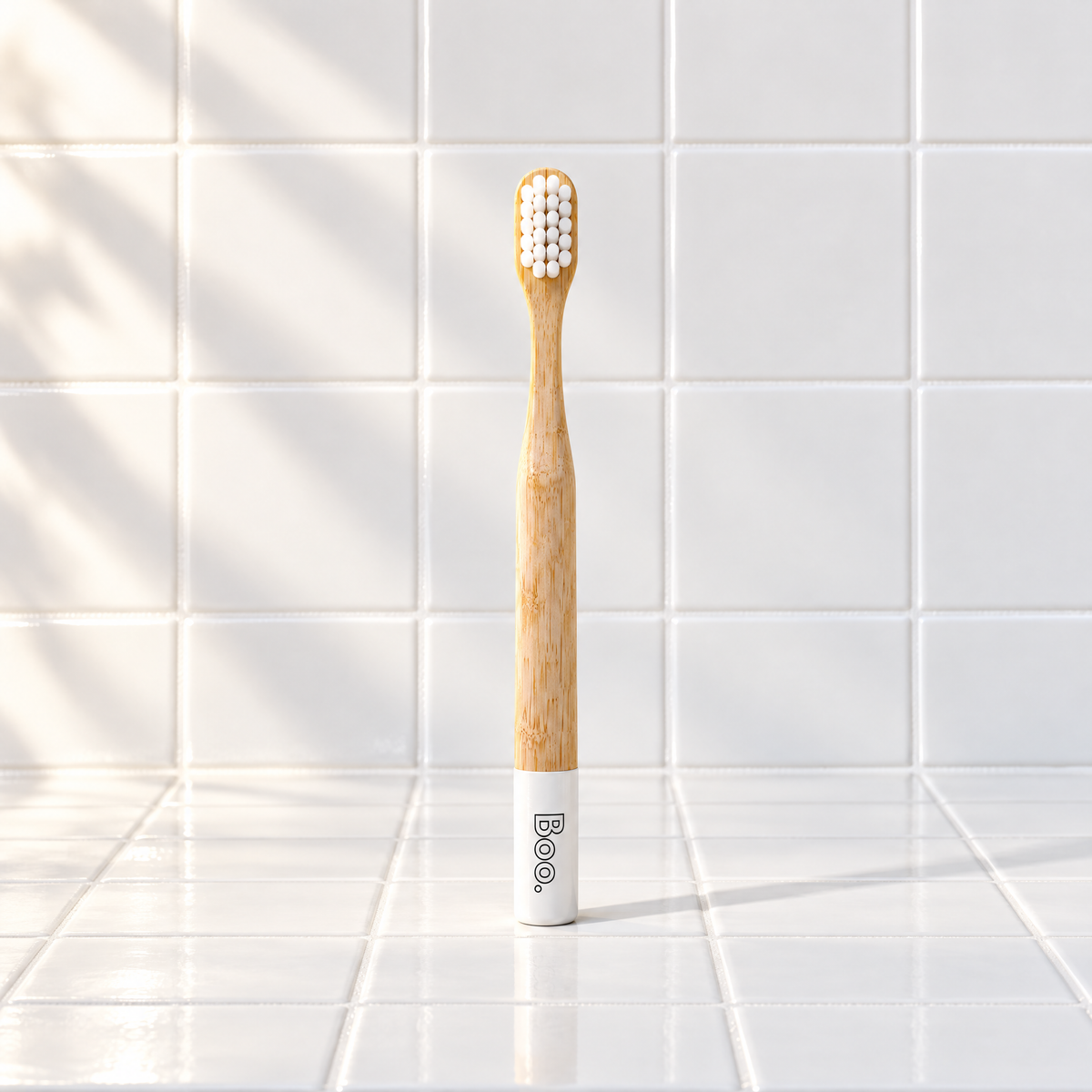 Boo kids bamboo toothbrush with white bristles and a white end cap, standing on white tiles