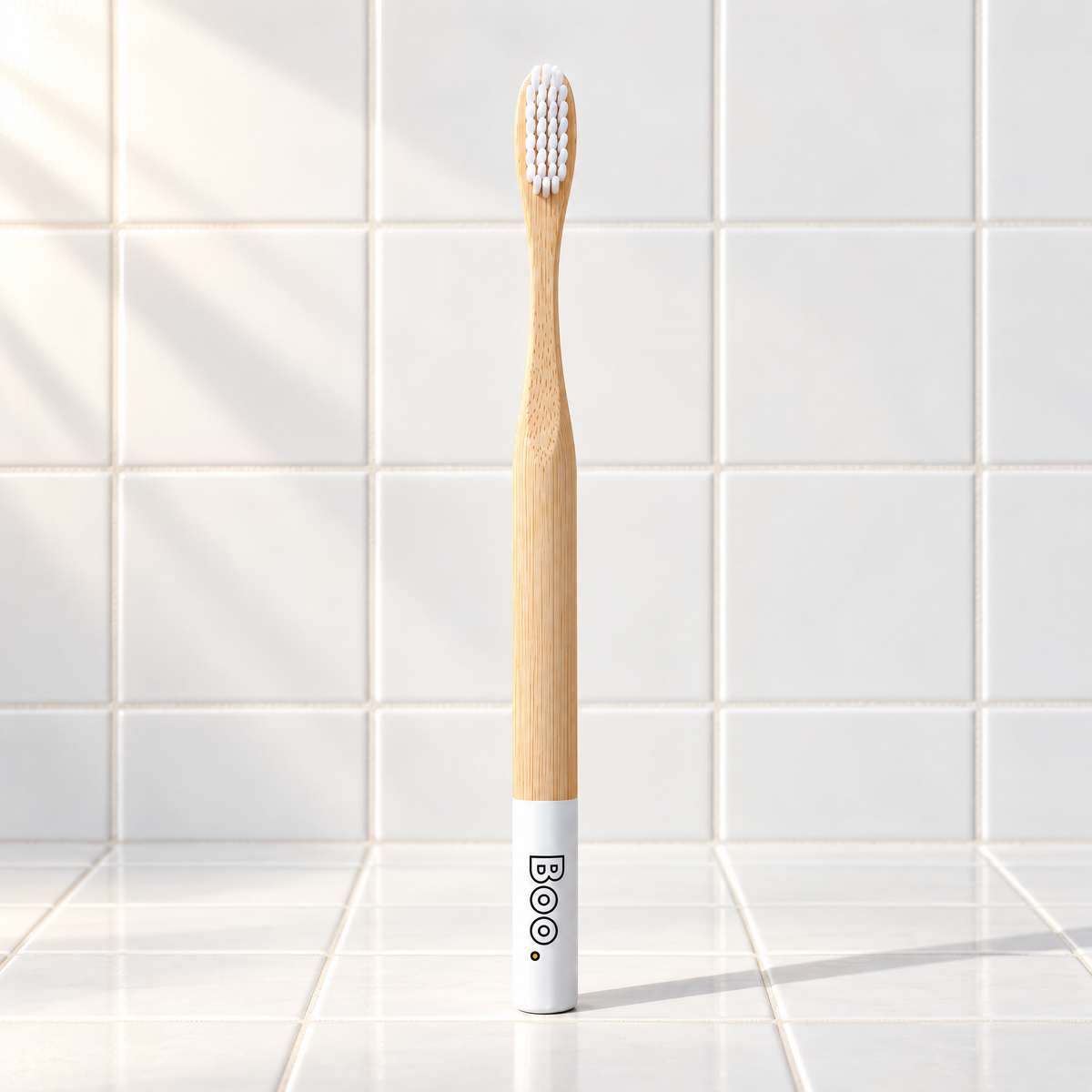Boo adult bamboo toothbrush with white bristles and a white end cap, standing on white tiles