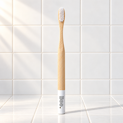 Boo adult bamboo toothbrush with white bristles and a white end cap, standing on white tiles