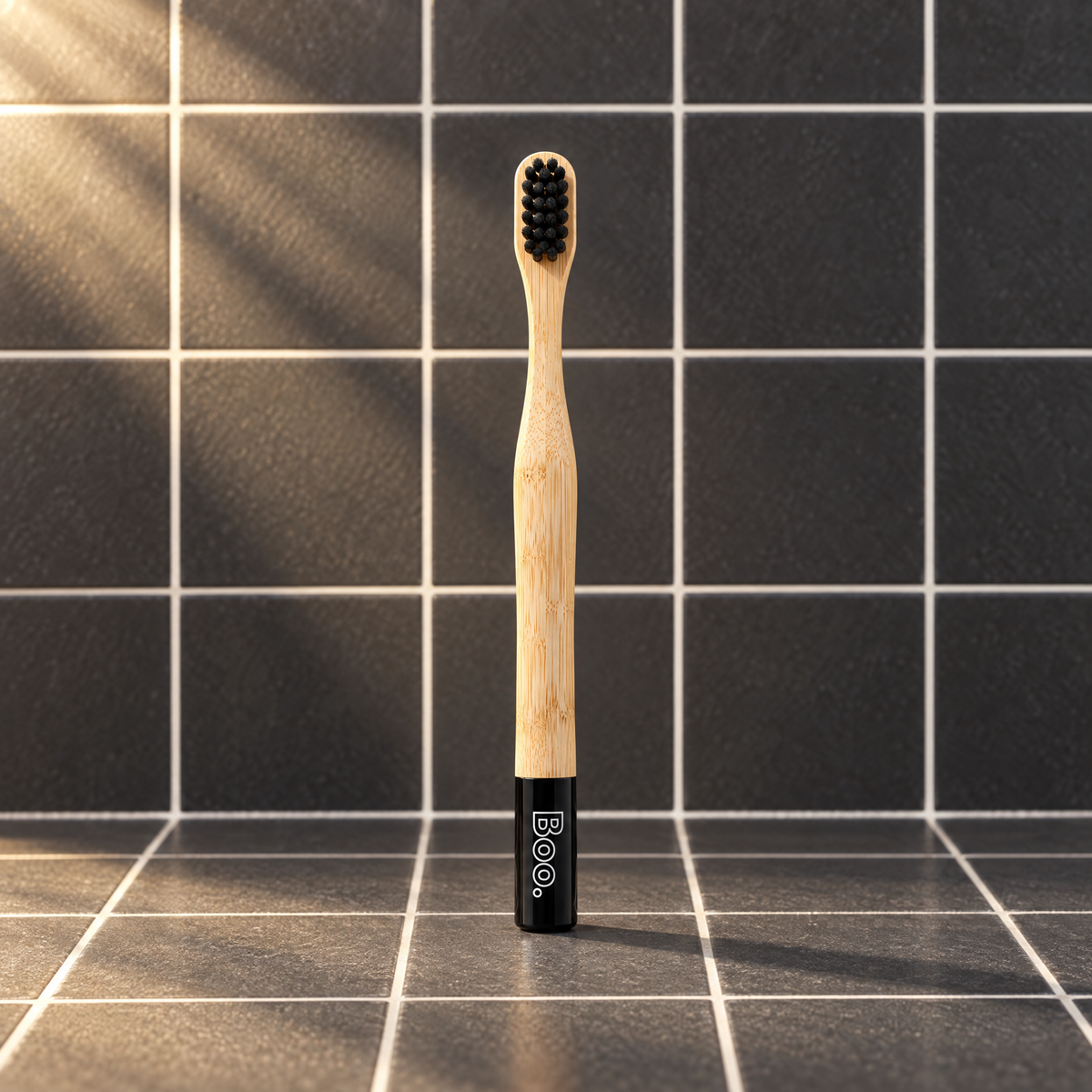 Boo kids bamboo toothbrush with black bristles and a black end cap, standing on charcoal tiles