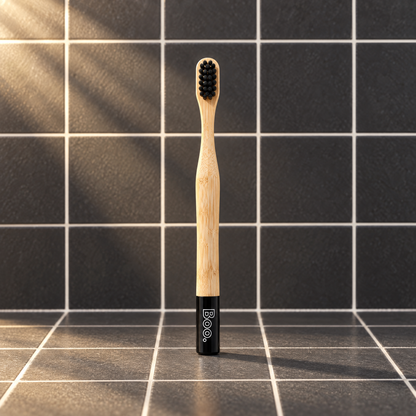 Boo kids bamboo toothbrush with black bristles and a black end cap, standing on charcoal tiles