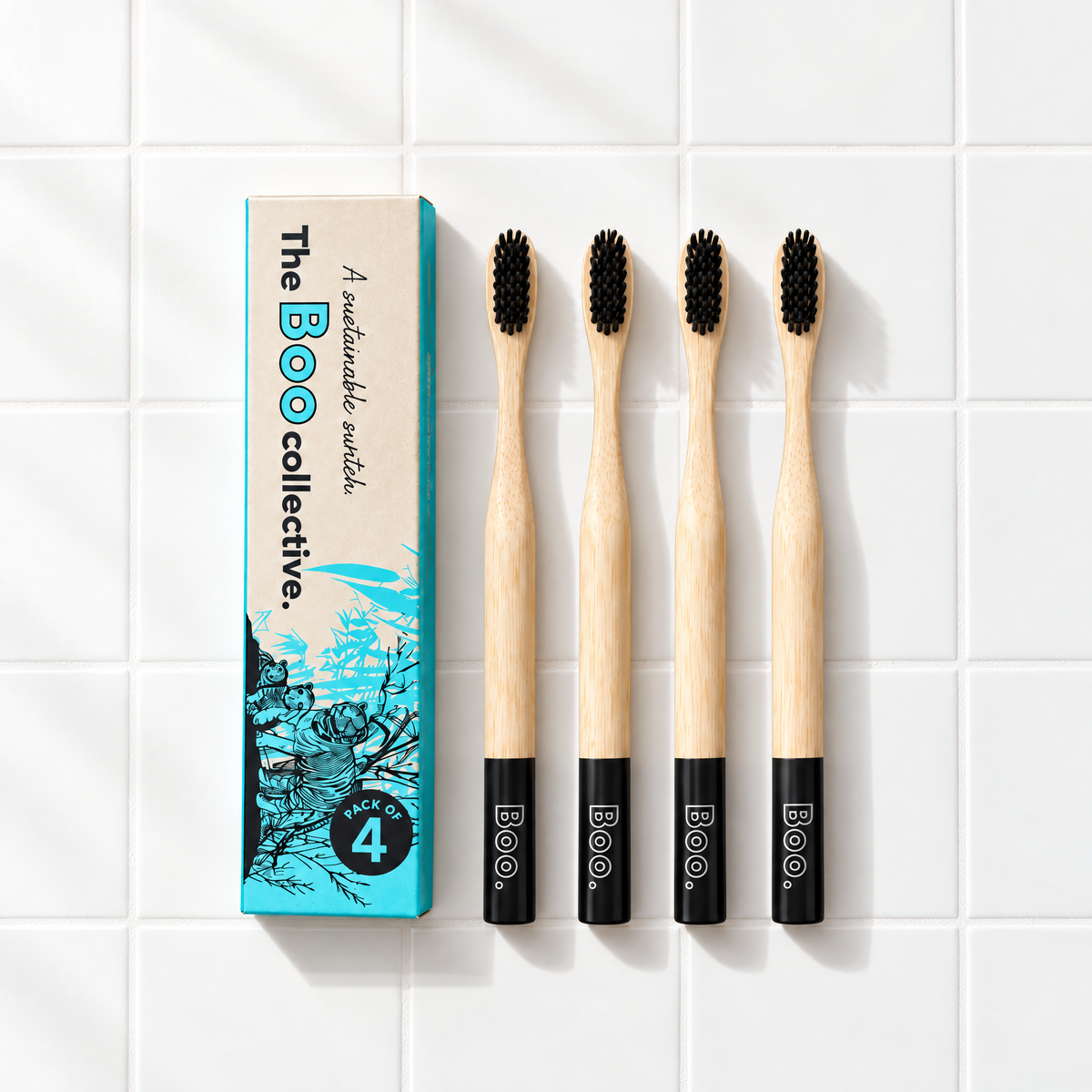 Four Boo adult bamboo toothbrushes with black bristles laid out beside the Boo four pack box
