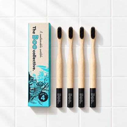 Four Boo adult bamboo toothbrushes with black bristles laid out beside the Boo four pack box