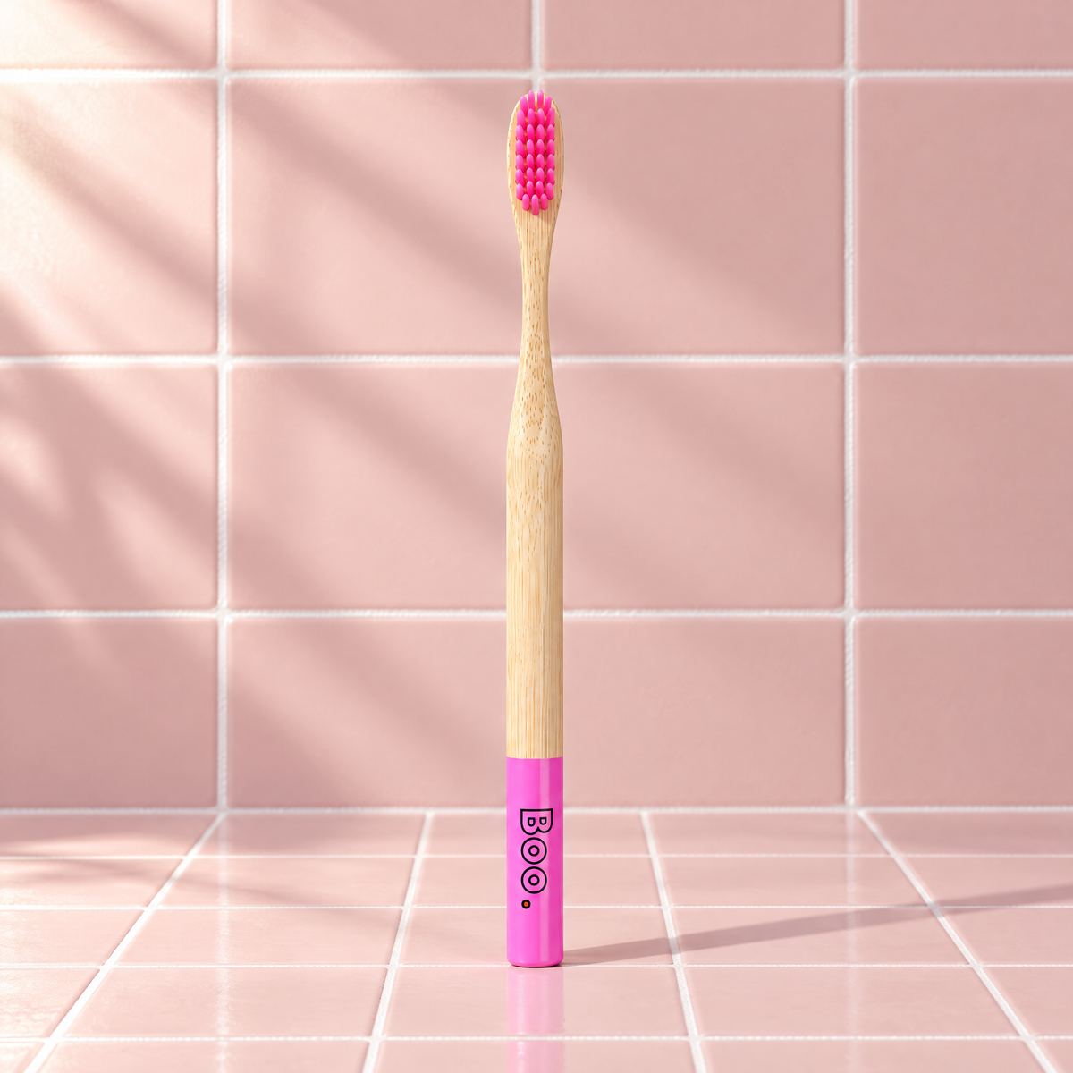 Boo adult bamboo toothbrush with pink bristles and a pink end cap, standing on pink tiles