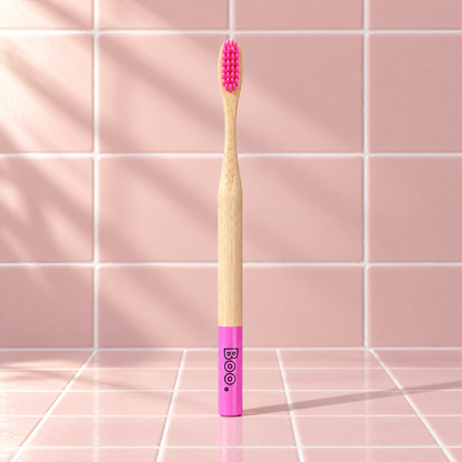 Boo adult bamboo toothbrush with pink bristles and a pink end cap, standing on pink tiles