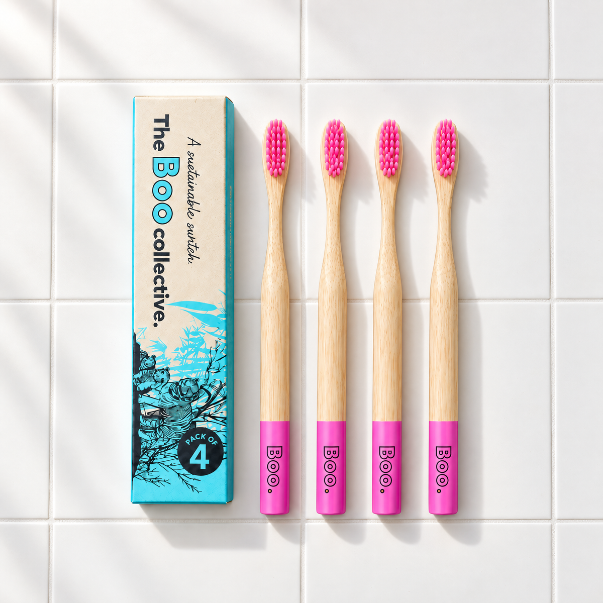 Four Boo adult bamboo toothbrushes with pink bristles laid out beside the Boo four pack box
