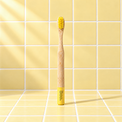 Boo kids bamboo toothbrush with yellow bristles and a yellow end cap, standing on yellow tiles